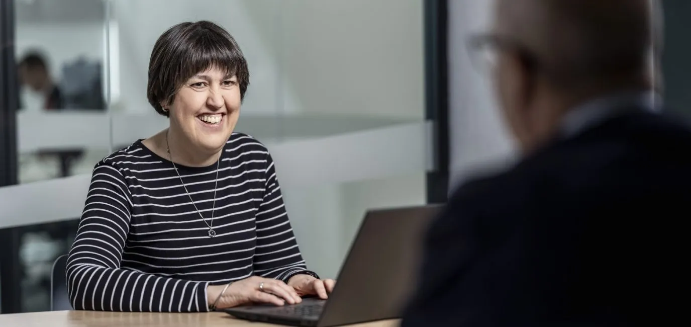 Mujer sonriendo, tomando datos frente a un candidato en una entrevista de trabajo.